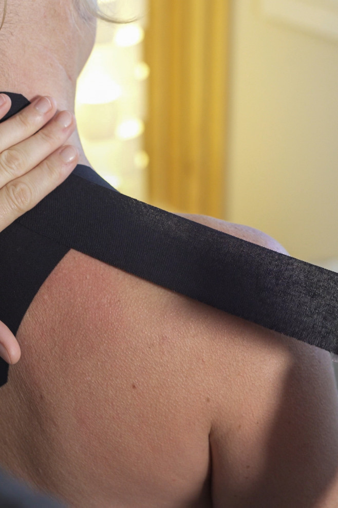 The therapist's gloved hands are resting on the patients shoulders, the patient is laying down on a massage table.