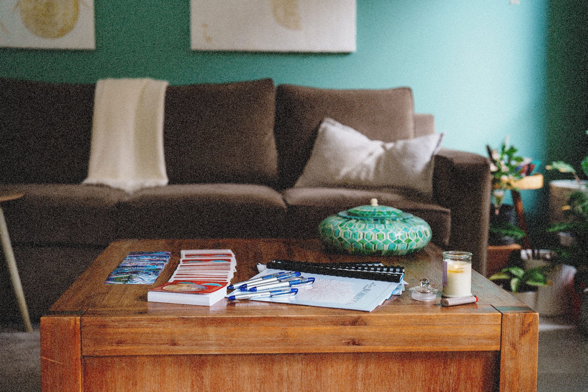 a peaceful, living room setting with a couch, coffee table and potted plants. On the table is some worksheets and an incense device