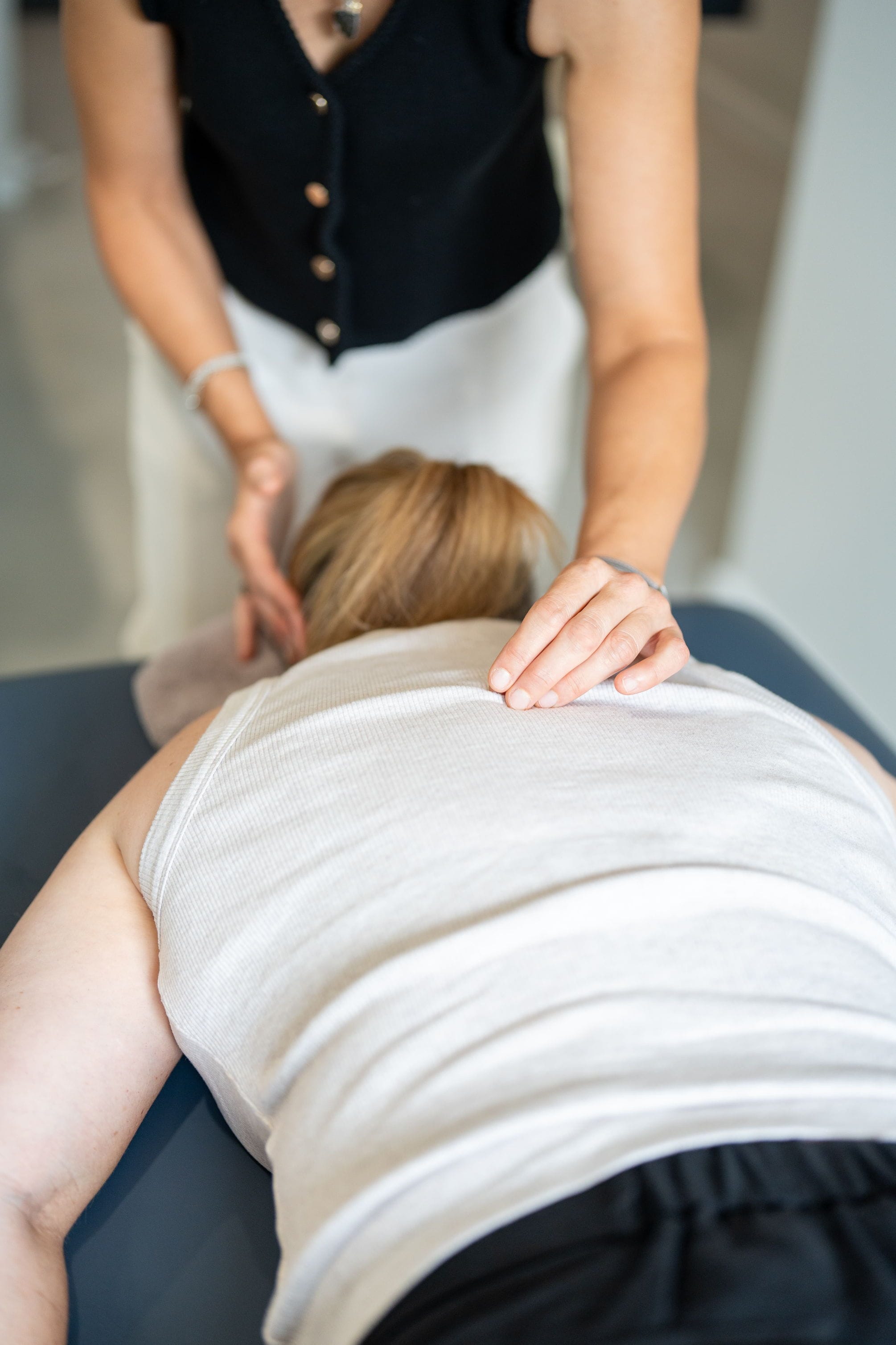 a women is giving a spinal flow massage treatment to a patient laying on a raised massage table. one hand is placed on her temple and the other on her upper spine