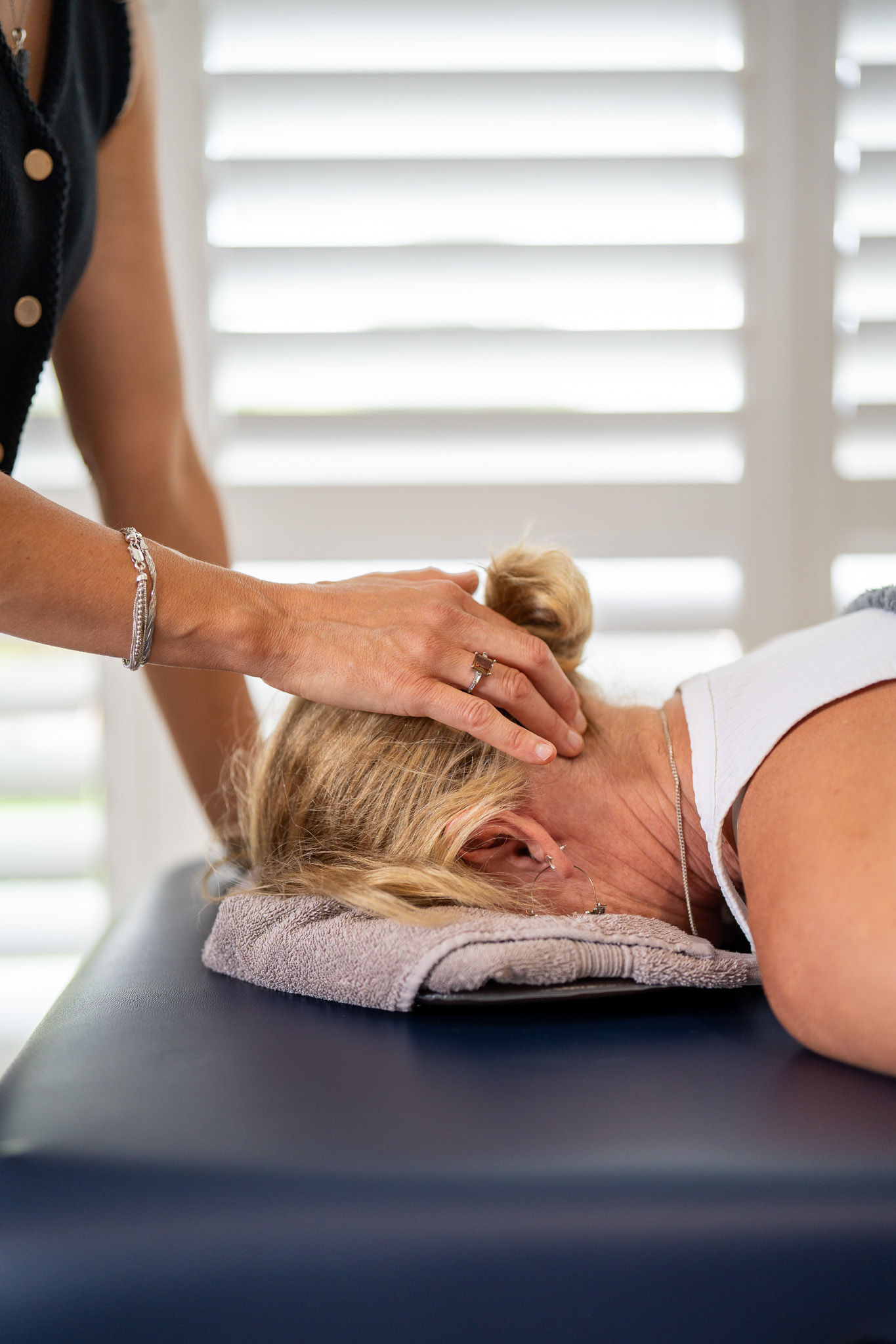 The therapist's hand is resting on the patients neck at the top of the spine, the patient is laying down on a massage table.