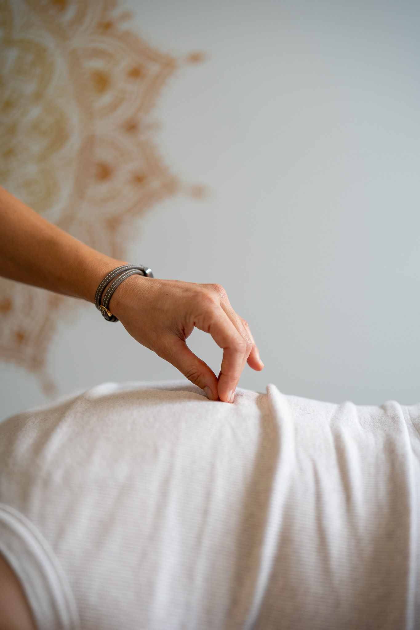 The therapist's hand is resting in a pinched shape on the patients spine at the middle of their back, the patient is laying down.
